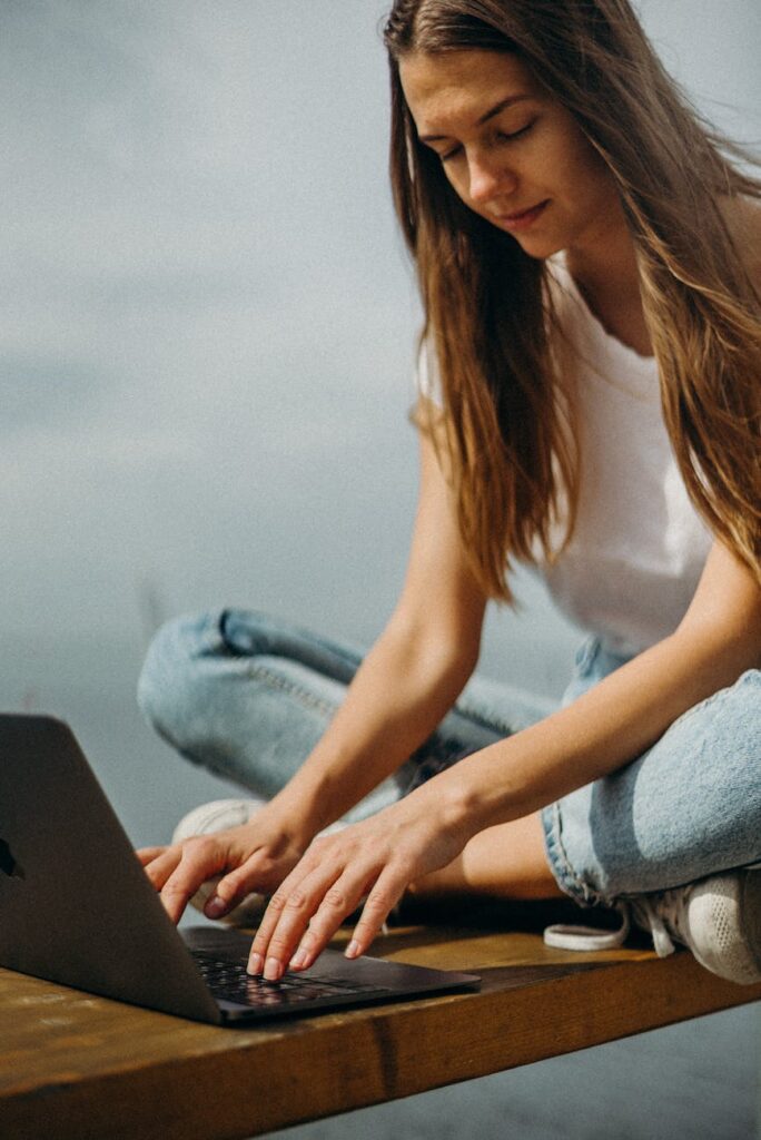 A young woman in casual clothes working remotely outdoors on a laptop.
