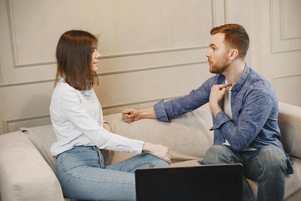 Terapia de Casal Online | Fortaleça seu Relacionamento A young couple engaged in a conversation while sitting on a beige couch indoors.